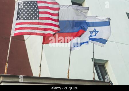 Amerikanische, russische und israelische Flaggen flattern an der Wand eines Gebäudes in Tel Aviv, Israel; Bewegungsunschärfe, selektiver Fokus Stockfoto