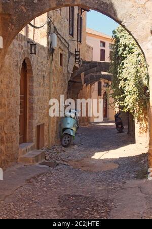 Typische ruhige gepflasterte Straße in rhodos Stadt mit alten gelb bemalten Häusern und einem Steinbogen mit sonnenbeschienenen Sommerhimmel Stockfoto