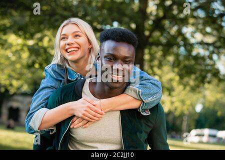 Eine Nahaufnahme von einem Mann, der eine Frau ein Huckepack heben durch einen Park. Sie sind beide lächelnd. Stockfoto