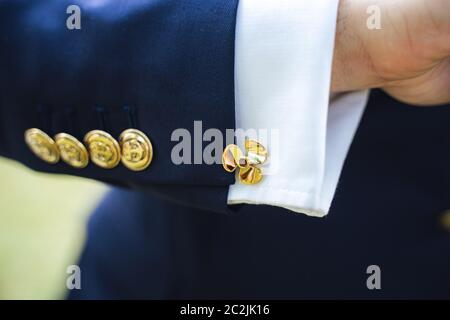 Nahaufnahme der Hand des Mannes mit goldenen Propeller Manschettenknöpfen auf dem Hemd und goldenen Knöpfen mit Anker Zeichen auf blauem Anzug. Mode, formelle Kleidung Konzept Stockfoto