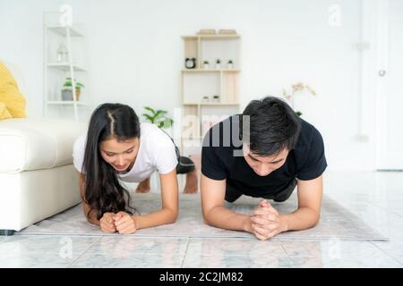 Asiatische junge Paar Mann und Frau in Sportkleidung tun Plank während des Trainings im Wohnzimmer zu Hause, um Übung in ihren Alltag zu bekommen, während SoC Stockfoto