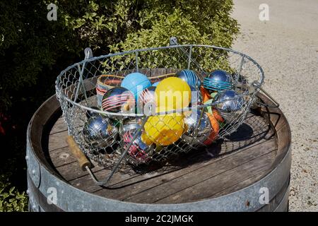 Bunte Petanque-Kugeln in einem Drahtkorb auf einem alten Holzweinfass, an einer Hecke, außerhalb von Chateau Hourtin-Ducasse, Saint-Sauveur, Frankreich Stockfoto