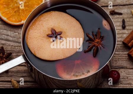 Kleiner Stepptopf mit Glühwein und Zimtstangen, Orangenscheibe und Apfel auf Holztisch Blick. Heißes Wintergetränk. Weihnachtsgetränk. Stockfoto