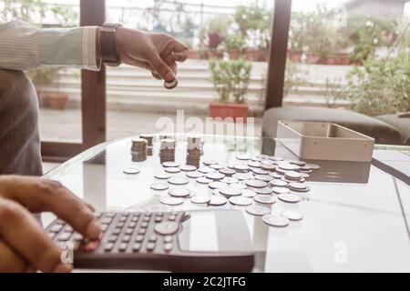 Bild des Geschäftsmannes Zählen von Münzen mit Rechner am Schreibtisch im Büro. Unternehmer Hand Münzen am Stack. Wirtschaft Finanzen Einsparungen und Investoren Stockfoto