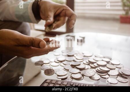Zugeschnittenes Bild des Geschäftsmannes Zählen von Münzen mit Rechner am Schreibtisch im Büro. Unternehmer Hand Zählen von Münzen. Wirtschaft Finanzen Einsparungen und Investoren Stockfoto