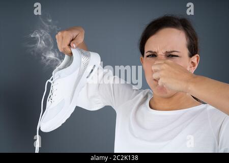 Nahaufnahme einer Frau, die Ihre Nase Halten stinkende Schuhe auf grauem Hintergrund Stockfoto