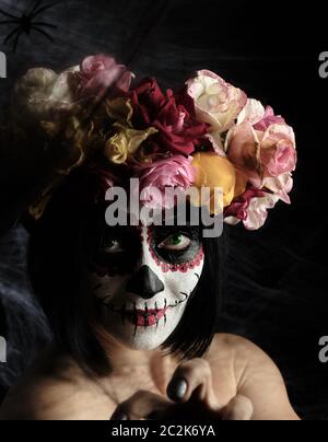 Mädchen mit schwarzen Haaren ist in einem Kranz von bunten Rosen und Make-up gekleidet ist auf Ihrem Gesicht Sugar Skull zum Tag der Toten, Nahaufnahme Stockfoto