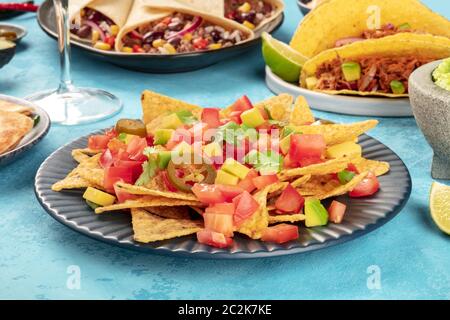 Nachos mit Avocado und Tomaten, mit jalapeno Pfeffer und Koriander Blätter, auf einem Tisch mit anderen mexikanischen Essen Stockfoto