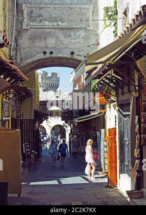 Eine Frau schaut sich ein Menü außerhalb eines Restaurants an, während Touristen mit Schiffen eine Straßenlinie entlang in der altstadt von rhodos gehen Stockfoto