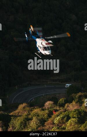 Ein Rettungshubschrauber MBB BK117 senkt die Ausrüstung an den Ort eines Autos, das an einem steilen Ufer auf der Dyers Pass Road, Christchurch, Neuseeland, herunterfiel Stockfoto