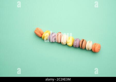 Runde bunte Macarons gebacken mit Sahne liegen in einer Linie auf einem grünen Hintergrund, Flach, kopieren Raum Stockfoto