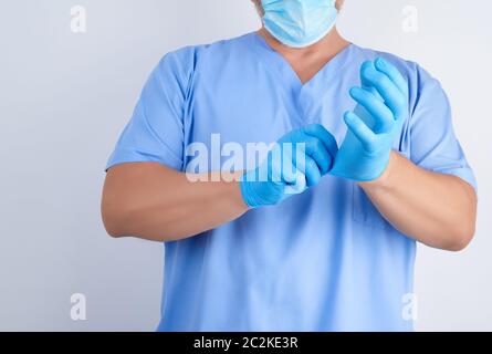 Männlicher Arzt in der blauen Uniform setzt auf seinen Händen weiß Sterile Latex Handschuhe vor der Operation, weißer Hintergrund Stockfoto