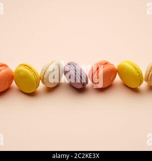 Runde bunte Macarons gebacken mit Sahne liegen in einer Linie auf einem beigen Hintergrund, kopieren Raum Stockfoto