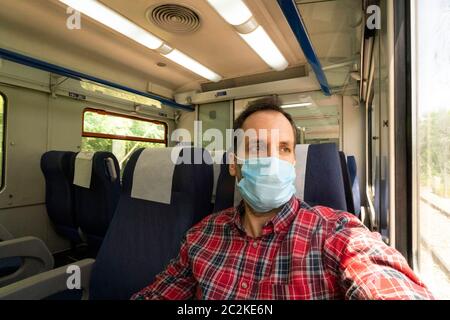 Mann in einem Zug mit Gesichtsmaske zum Schutz während der neuartigen Coronavirus COVID-19 Pandemie Stockfoto