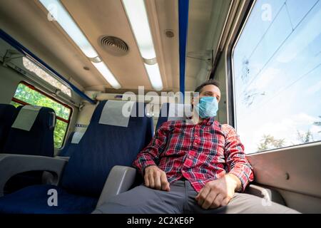 Mann in einem Zug mit Gesichtsmaske zum Schutz während der neuartigen Coronavirus COVID-19 Pandemie Stockfoto