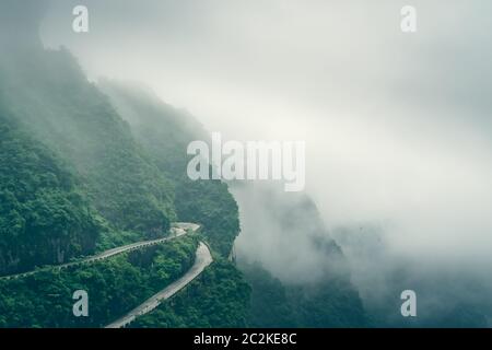 Durch niedrige Wolken und Nebel gefährlich scharfe Kurven auf der kurvenreichen Straße von 99 wendet sich an die Spitze der Tianmen Mountain, Zhangjiajie Nationalpark, Hu abgedeckt Stockfoto