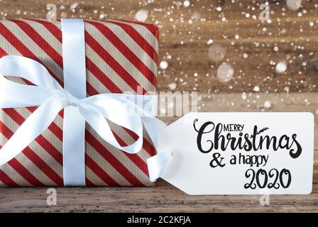 Ein Weihnachtsgeschenk mit Label mit Egnlish Kalligraphie frohe Weihnachten und einen guten Rutsch ins Jahr 2020. Geschenkpapier mit Schleife und Schneeflocken Stockfoto