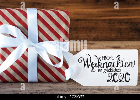 Ein Weihnachtsgeschenk mit Label mit Deutschen Kalligraphie Frohe Weihnachten und ein Glueckliches 2020 bedeutet, frohe Weihnachten und einen guten Rutsch ins Jahr 2020. Verpackung Pap Stockfoto