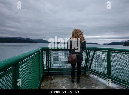 Eine Frau steht auf der Aussichtsplattform einer Washington State Ferry, während sie durch die San Juan Insel, Washington State, USA segelt. Stockfoto