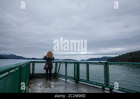 Eine Frau steht auf der Aussichtsplattform eine Washington State Ferry, die ein Foto macht, während sie durch die San Juan Inseln, Washington, USA segelt. Stockfoto