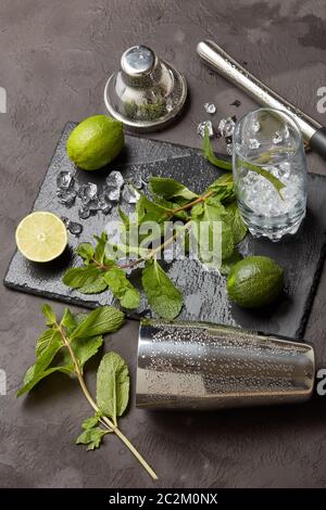 Set von Bar-Tools: Cocktail Shaker, Muddler und Glas mit Eis, Limette und Minze auf dunklen Stein Tisch. Draufsicht. Werkzeug des Barkeepers. Mojito Cocktailzubereitung Stockfoto