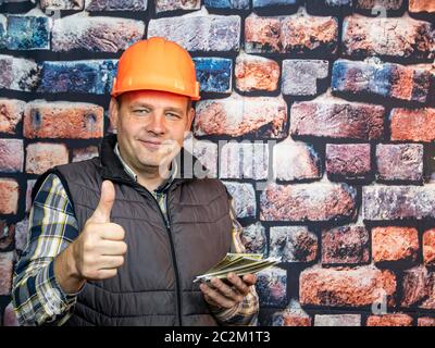 Arbeitnehmer in einem orange Helm mit Geld in der Hand. Menschen. Lohn. Stockfoto