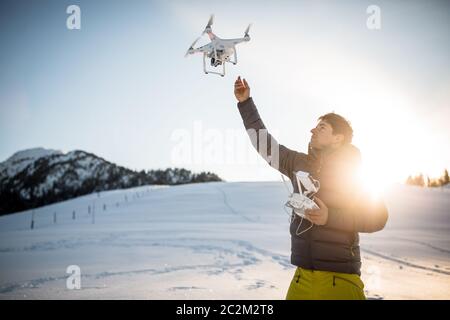 Junger Mann, der seine Drohne im verschneiten Freien kontrolliert. Drohnenbetreiber hält einen Sender und landet mit einer Drohne. Stockfoto