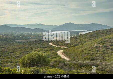 Die hügelige Landschaft, die typisch für die Küste im Süden von Sardinien mit einer Schmutz Weg flussabwärts Richtung Meer. Stockfoto