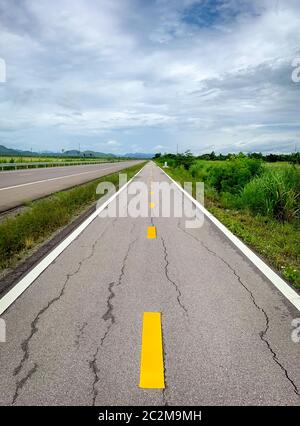 Perspektive Risse im Asphalt Weg auf den Berg. Lange Gerade beschädigt asphaltierte Straße. Schlechte Oberfläche der Radweg und weißen Himmel und Wolken mit gre Stockfoto