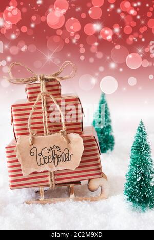 Schlitten mit Weihnachtsgeschenk und Label mit englischen Kalligraphie Happy Weekend. Weihnachtsbaum mit Schnee und rote Sekt Hintergrund Stockfoto