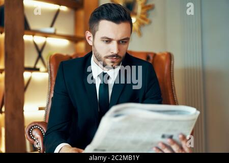 Selbstbewusster junger Geschäftsmann beim Lesen von Zeitungen und aktuellen Nachrichten im Sessel Stockfoto