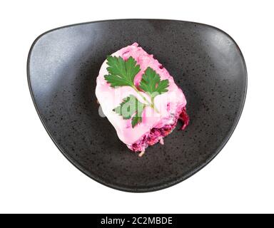 Draufsicht über die Portion Des Gekleideten Herings russischen Salats, dekoriert mit Petersilienblatt auf schwarzem Teller isoliert auf weißem Hintergrund Stockfoto