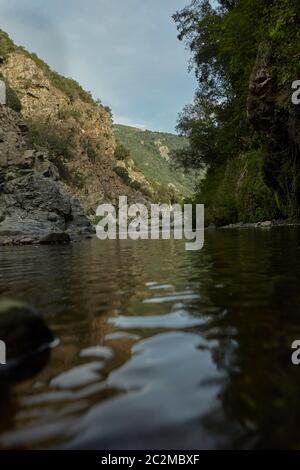 Felswand mit Vegetation bedeckt ist, die Grenze der Wasserlauf in den Bergen mit verschiedenen Felsen, die aus dem Wasser steigen: Die Ansicht von Sa Stid Stockfoto
