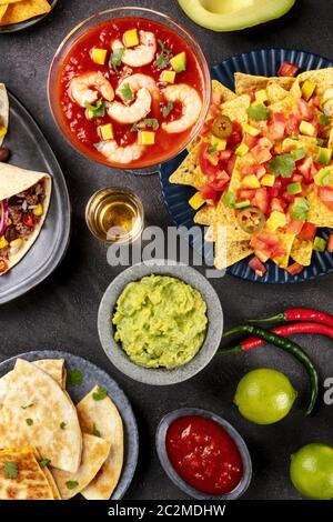 Mexikanisches Essen, viele Gerichte der Küche von Mexiko, Flatlay, Top-Shot auf schwarzem Hintergrund. Nachos, Tequila, Guacamole, Garnelen Stockfoto