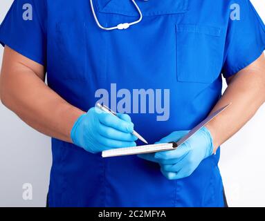 Arzt in der blauen Uniform und sterile Latex Handschuhe holding Öffnen leer Notebook, weißer Hintergrund, schreibt mit seiner rechten Hand Stockfoto