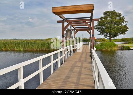 Kleine hölzerne Zugbrücke über eine Kanalwindmühle im Hintergrund, holländische Landschaft Stockfoto