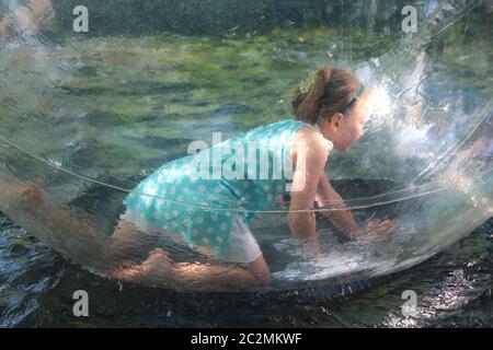 Kleine Mädchen spielen für ein Laufwerk in transparenten Sphäre. Kinder spielen auf dem Wasser. Glückliche Kindheit Stockfoto