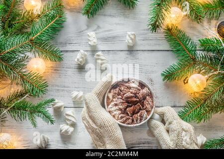 Die Frau Hände in Wolle Handschuhe Holding eine Tasse heiße Schokolade mit Marshmallows mit geschmückten Weihnachtsbaum Niederlassungen Stockfoto