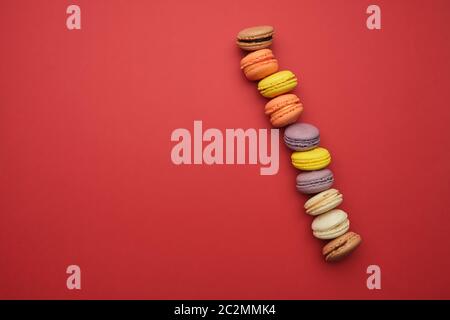 Runde bunte Macarons gebacken mit Sahne liegen in einer Linie auf einem roten Hintergrund, Flach, kopieren Raum Stockfoto