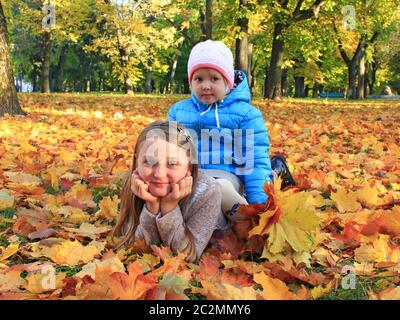 Junge hübsche Schwestern legen sich im Herbstpark auf gelben Blättern. Kleine Kinder mit Herbstblättern Stockfoto