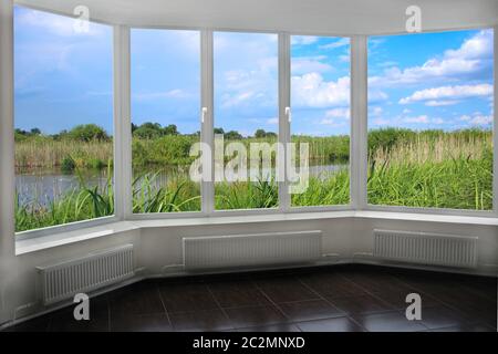 Zimmer mit großem Fenster mit Blick auf die Landschaft mit See mit Gehstock umgeben. Blick vom Zimmerfenster Stockfoto