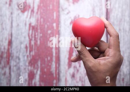 Mann hält rotes Herz in den Händen auf Holztisch. Stockfoto