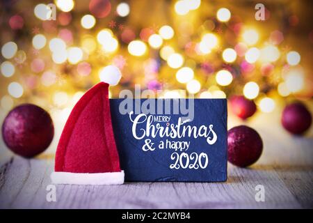Sighn Wth English Kalligraphie Frohe Weihnachten und guten Rutsch ins Jahr 2020. Purple Christmas Ball Ornament mit rote Weihnachtsmütze. Funkelnden Lichtern Hintergrund Stockfoto