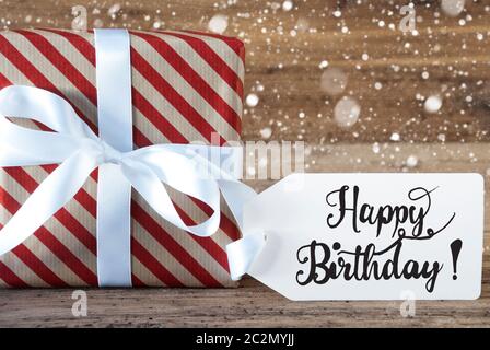 Ein Weihnachtsgeschenk mit Label mit Egnlish Kalligraphie Happy Birthday. Geschenkpapier mit Schleife und Schneeflocken Stockfoto