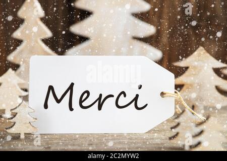 Etikett mit französischen Text Merci bedeutet. Vielen Dank. Weiß Holz- Weihnachten Baum als Dekoration. Braun Holz- Hintergrund mit Schnee Stockfoto