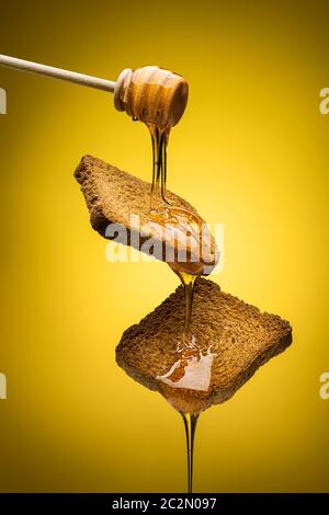 Honig tropft aus Holz-Dipper auf zwei Vollkornrusken. Stockfoto