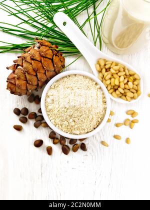 Zedernmehl in einer Schüssel, Nüsse und Kegel, Löffel mit geschälten Nüssen, grüner Kiefernzweig und Zedernmilch in einer Flasche auf Holzbretthintergrund von oben Stockfoto