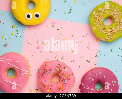 Ganze runde rosa Donuts mit bunten Streuseln liegen auf einer blau-rosa Hintergrund, Ansicht von oben, Pastellfarben Stockfoto