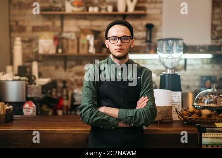 Barkeeper in schwarzer Schürze steht gegen Barzähler. Kaffeehaus Küche auf dem Hintergrund. Stockfoto