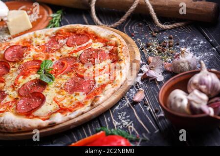 Pizza mit Wurst und Tomaten in der Nähe von Gewürzen. Poster für Restaurants oder Pizzerien. Pizza auf schwarzem Hintergrund Stockfoto